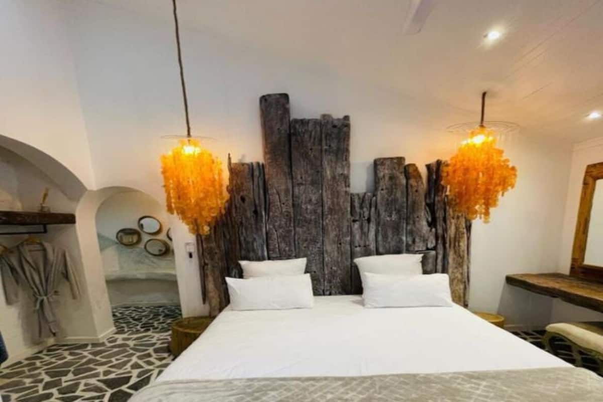 A bedroom with a large bed, two hanging orange lamps, and a rustic wooden headboard.