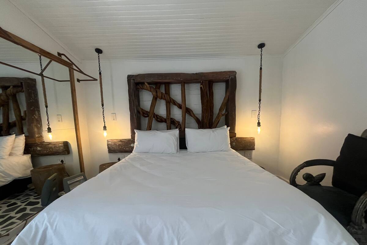 A bedroom with a large bed, wooden headboard, hanging lights, and a chair.