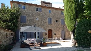 A stone building with a courtyard featuring outdoor seating and a pergola. - Le Mas Pacha (L'Isle-sur-la-Sorgue)