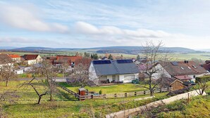 A rural village with houses, a fenced yard, and a view of distant hills.
