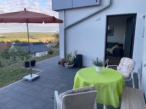 An outdoor patio with a table and chairs, a red umbrella, and potted plants. - Apartment 'Am Rothen Hang' with Mountain View, Private Terrace and Wi-Fi (Oberelsbach)