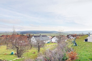 A rural landscape with houses, a grassy field, and a distant view of hills. - Apartment 'Am Rothen Hang' with Mountain View, Private Terrace and Wi-Fi (Oberelsbach)