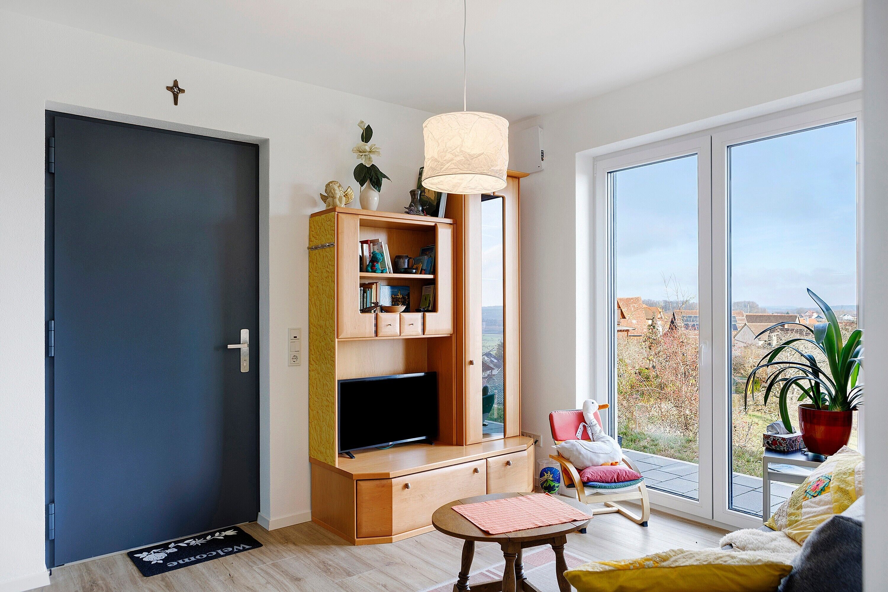 Una sala moderna con televisor, mueble de entretenimiento de madera, una mesita, una silla y un ventanal con vistas.