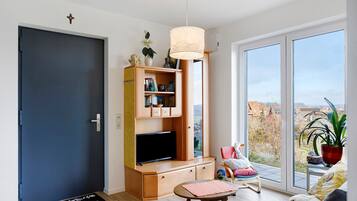 Una sala moderna con televisor, mueble de entretenimiento de madera, una mesita, una silla y un ventanal con vistas.
