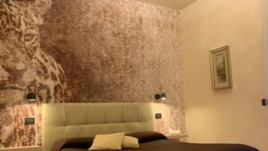 A bedroom with a bed, a nightstand, a chair, and a wall with a textured pattern. - Pernice77 (Sulzano)
