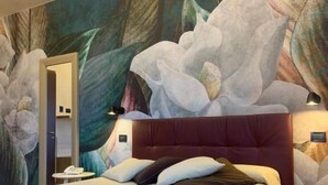 A modern hotel room with a large bed, a curved headboard, and a wall mural of flowers. - Pernice77 (Sulzano)