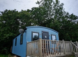 A small blue cabin with a wooden deck and a satellite dish.