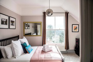 Un dormitorio con cama, un espejo, una ventana con cortinas e imágenes enmarcadas en la pared.