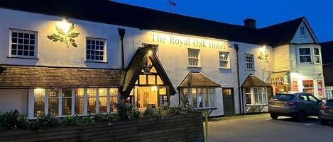 The Royal Oak Hotel with a traditional facade, large windows, and a well-lit entrance.