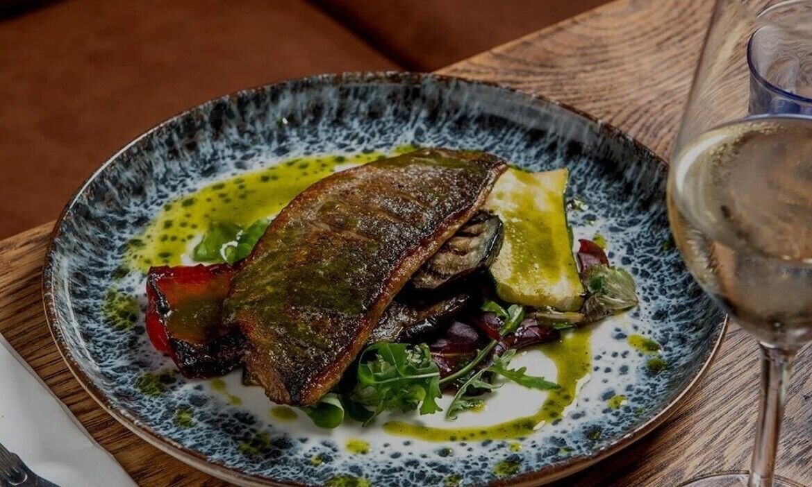 Un plato de comida con pescado, vegetales verdes y una copa de vino sobre una mesa.