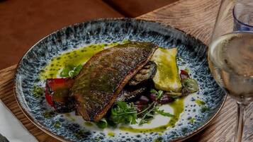 Un plato de comida con pescado, vegetales verdes y una copa de vino sobre una mesa.