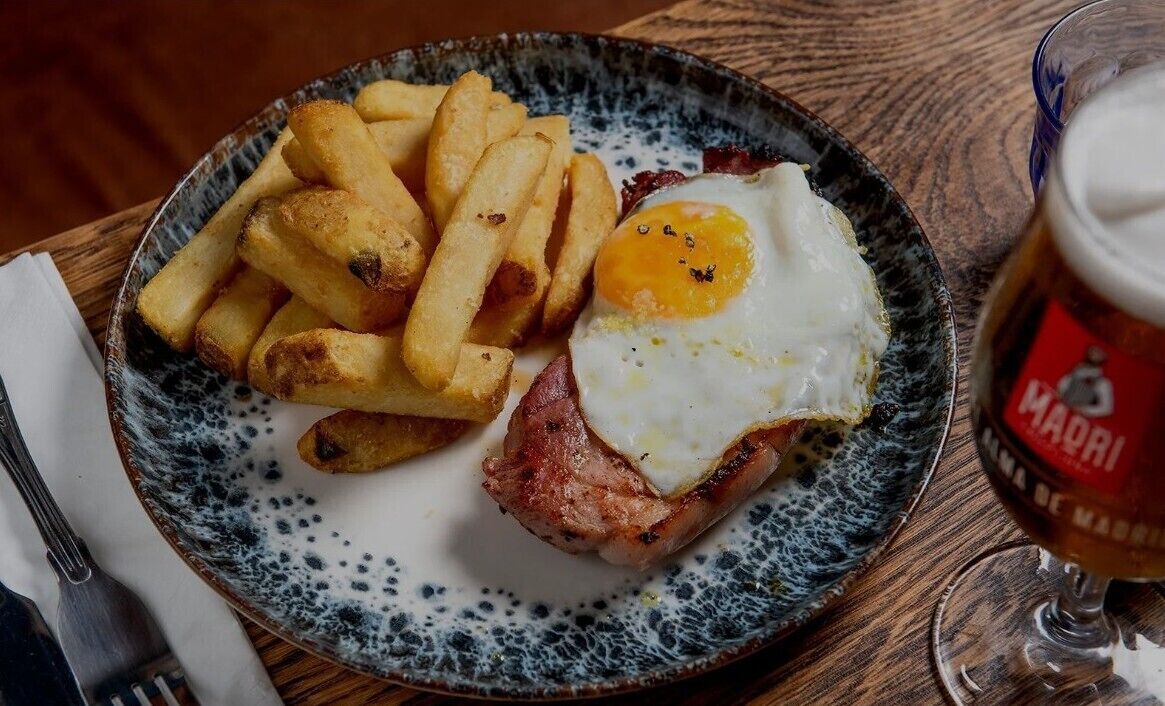 A plate with French fries, a fried egg, and a slice of ham.