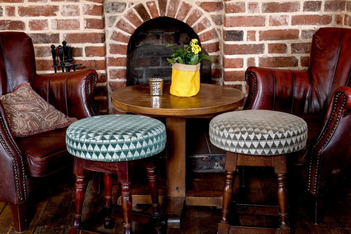 A brick fireplace, leather armchairs, and ottomans with patterned cushions.