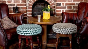 A brick fireplace, leather armchairs, and ottomans with patterned cushions.