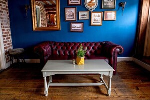 Una habitación con una pared azul oscuro, un sofá de cuero rojo, una mesa blanca y cuadros enmarcados.