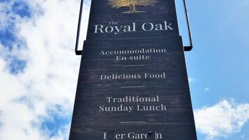 Letrero de The Royal Oak, destacando servicios como alojamiento, baño privado, comida deliciosa, almuerzo dominical tradicional y un jardín.