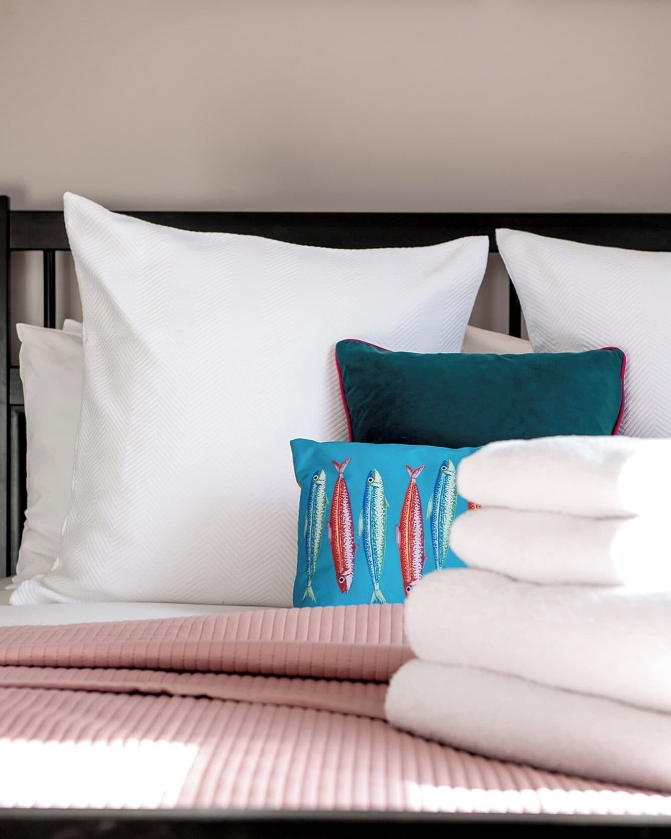 Un lit bien fait, avec des oreillers blancs et turquoise, une couverture rose et une tête de lit noire.