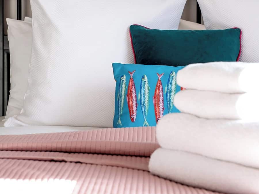 Cama bem arrumada com almofadas brancas e azul-esverdeadas, um cobertor rosa e uma cabeceira preta.