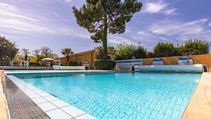 A swimming pool with clear blue water, surrounded by a tiled deck and a wooden fence.