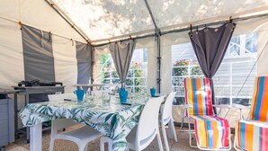 A tented outdoor area with a table set for dining, white chairs, and colorful beach chairs.