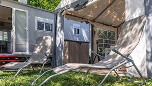 A camping area with a tent, a trailer, and two lawn chairs.