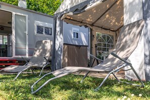 Un espace de camping comprenant une tente, une remorque et deux chaises de jardin.