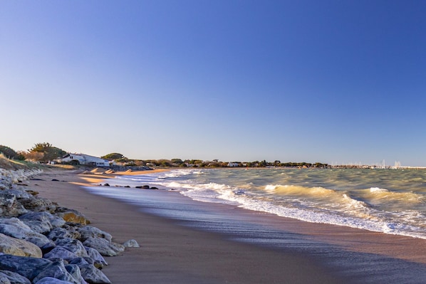 Une plage bordée de rochers, avec des vagues et une vue lointaine sur une ville.
