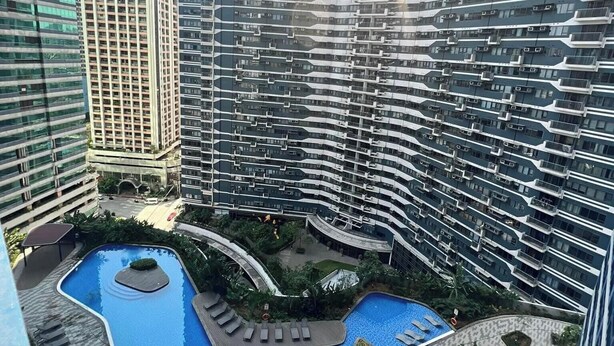 A high-rise building complex with a central courtyard featuring a swimming pool and lounge areas. - Cozy crib @ Air Residences -Makati (Makati)
