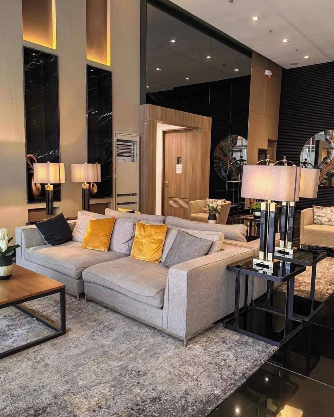 Ein modernes Wohnzimmer mit einem grauen Sofa, zwei Beistelltischen mit Lampen, einem Couchtisch und einem großen Spiegel.