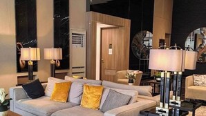 A modern living room with a grey sofa, two side tables with lamps, a coffee table, and a large mirror. - Cozy crib @ Air Residences -Makati (Makati)