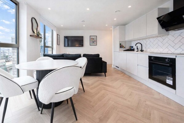 A modern kitchen with white cabinetry, a built-in oven, and a dining area with a round table and chairs.