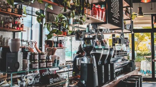 En caféindretning med hylder fyldt med forskellige varer, en kaffemaskine og hængende planter.