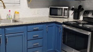 Una cocina con armarios azules, microondas, estufa y pileta.