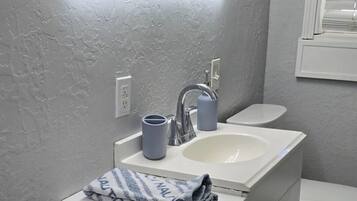 Ein Badezimmer mit weißem Waschtisch, einem Waschbecken, einem Spiegel mit Beleuchtung und einer Toilette.