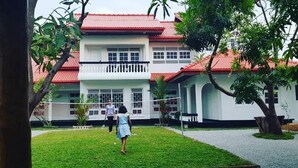 A two-story building with a red roof and white walls, surrounded by a well-maintained lawn and trees. - BEDBOX (Dambulla,)