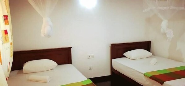 Une chambre avec deux lits simples, chacun doté d’une tête de lit en bois et de draps blancs.
