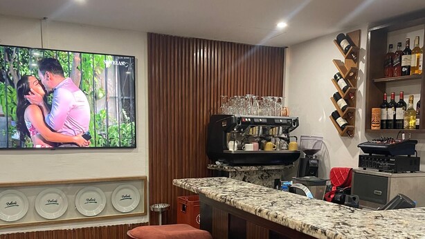 Eine moderne Küche mit Bar, einem Fernseher, der ein Paar zeigt, und Weinflaschen in Regalen.