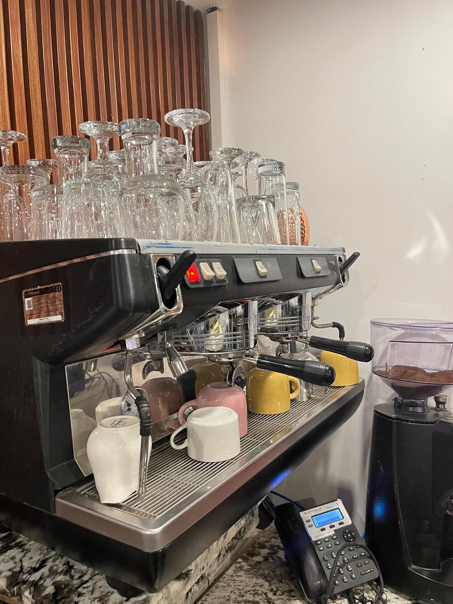 An espresso machine with multiple coffee cups and a phone.