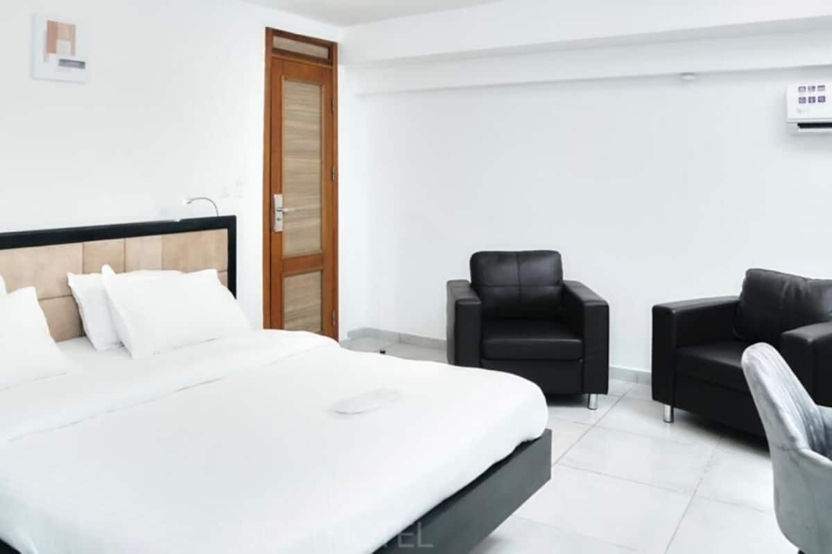 Camera d'albergo con un letto grande, due sedie nere, una porta in legno e un parete bianca.