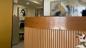 Ein Empfangsschalter mit Holzoptik, ein gerahmtes Kunstwerk darüber und ein kleiner Kühlschrank im Hintergrund.