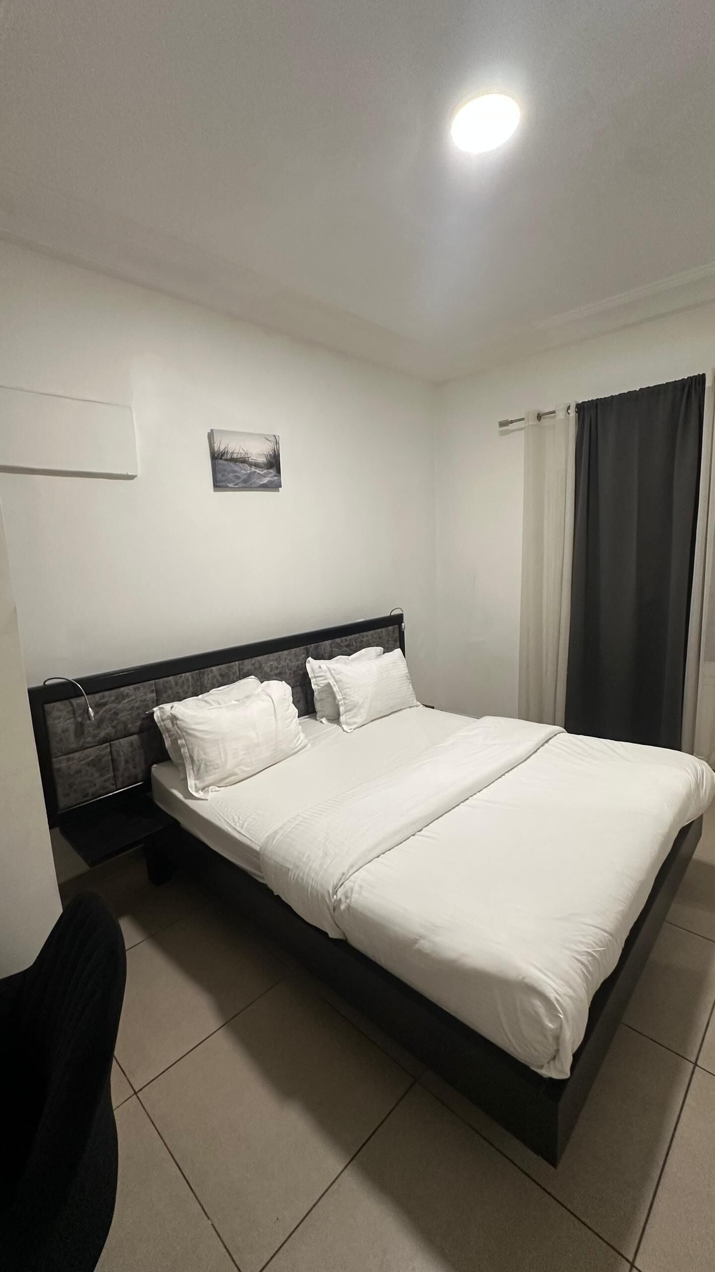 A neatly made bed with white linens, a headboard, and a small bedside table with a lamp.