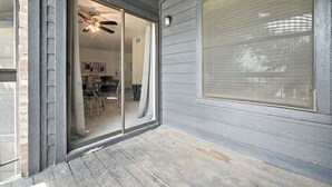 A sliding glass door leading into a room with a ceiling fan, a dining area with chairs, and a window with blinds.