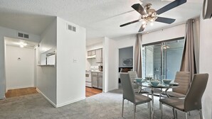 A modern apartment with a dining area featuring a round table and four chairs, a ceiling fan, and a view through a large window.