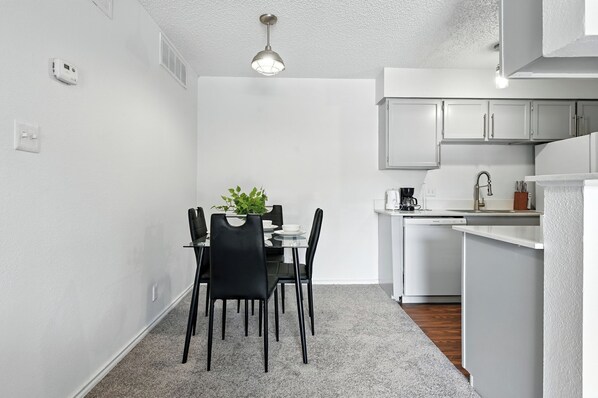 A compact kitchen with white cabinets, a dining area with a table and chairs, and a small island with a coffee machine.