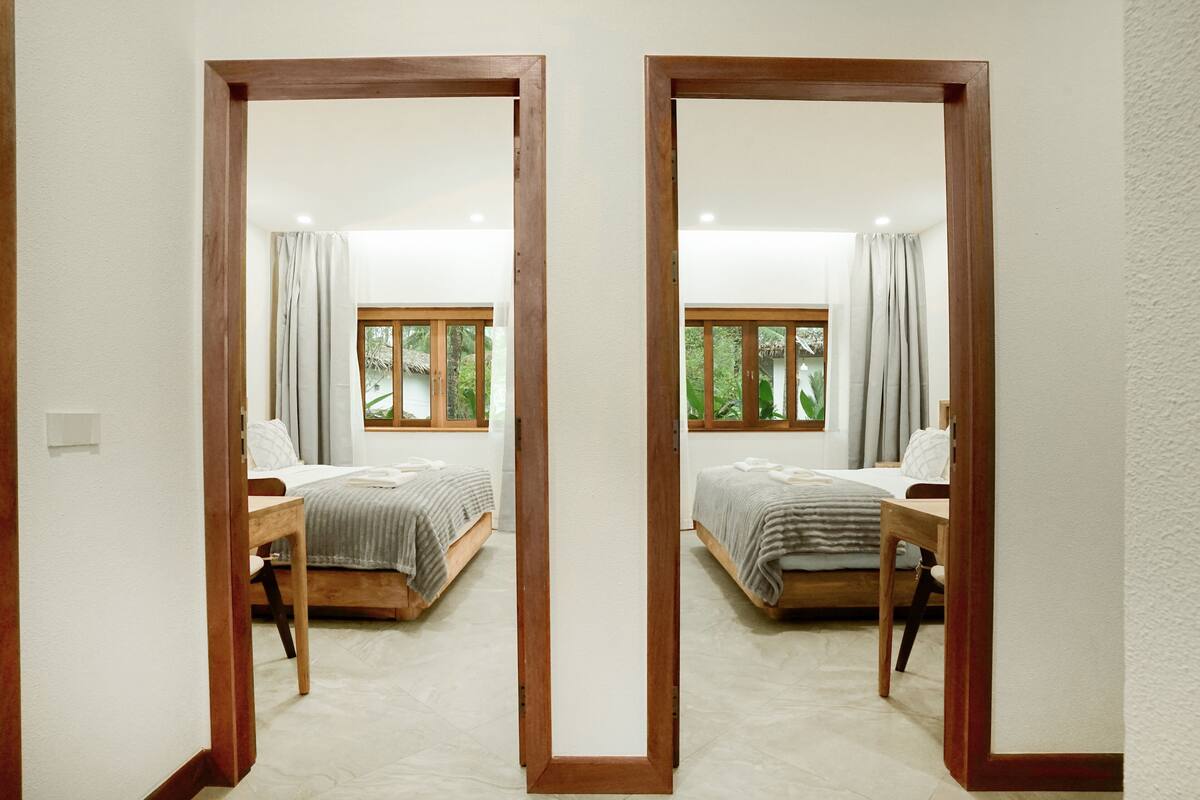 Une vue en miroir d’une chambre à coucher avec deux lits, un cadre en bois et une fenêtre avec des rideaux.