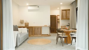 Una sala de estar moderna con sofá, una mesa de comedor con sillas, una zona de cocina con armarios de madera y un gran ventanal con cortinas.