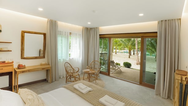 Habitación de hotel con una cama grande, un escritorio, una silla y un balcón con vista a palmeras.