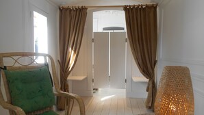 A room with a wicker chair, a green cushion, a woven floor lamp, and a view through a door with curtains. - Chambre d'hôte .Lodge Jardin Secret - cosy accommodation with breakfast (Arlanc)