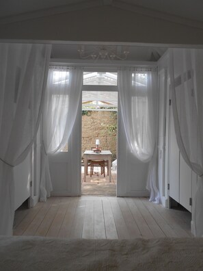 A room with a wooden floor, white curtains, and a table with chairs outside. - Chambre d'hôte .Lodge Jardin Secret - cosy accommodation with breakfast (Arlanc)