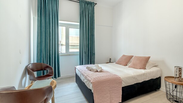 Ein Schlafzimmer mit einem Bett, einem Sessel, einem Fenster und Vorhängen.